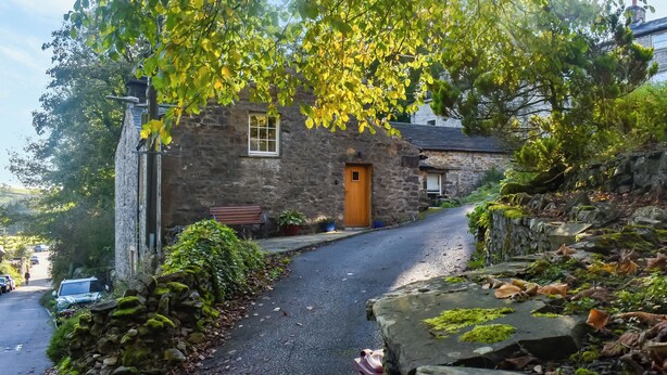 A stone house with a wooden door, a gravel driveway, and a stone wall with moss. - 1 bedroom accommodation in Slaidburn (Slaidburn)
