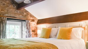 A bedroom with a large bed, a stone wall, a wooden ceiling, and a window with curtains. - 1 bedroom accommodation in Slaidburn (Slaidburn)