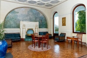 A room with a fireplace, round table, and chairs, a large arched window, and a mural on the wall. - Studio Apartment 'Au Temps Suspendu' with Mountain View, Balcony and Wi-Fi (Aix les Bains)