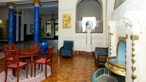 A lobby with a round wooden table, blue chairs, a blue armchair, and a large vase.