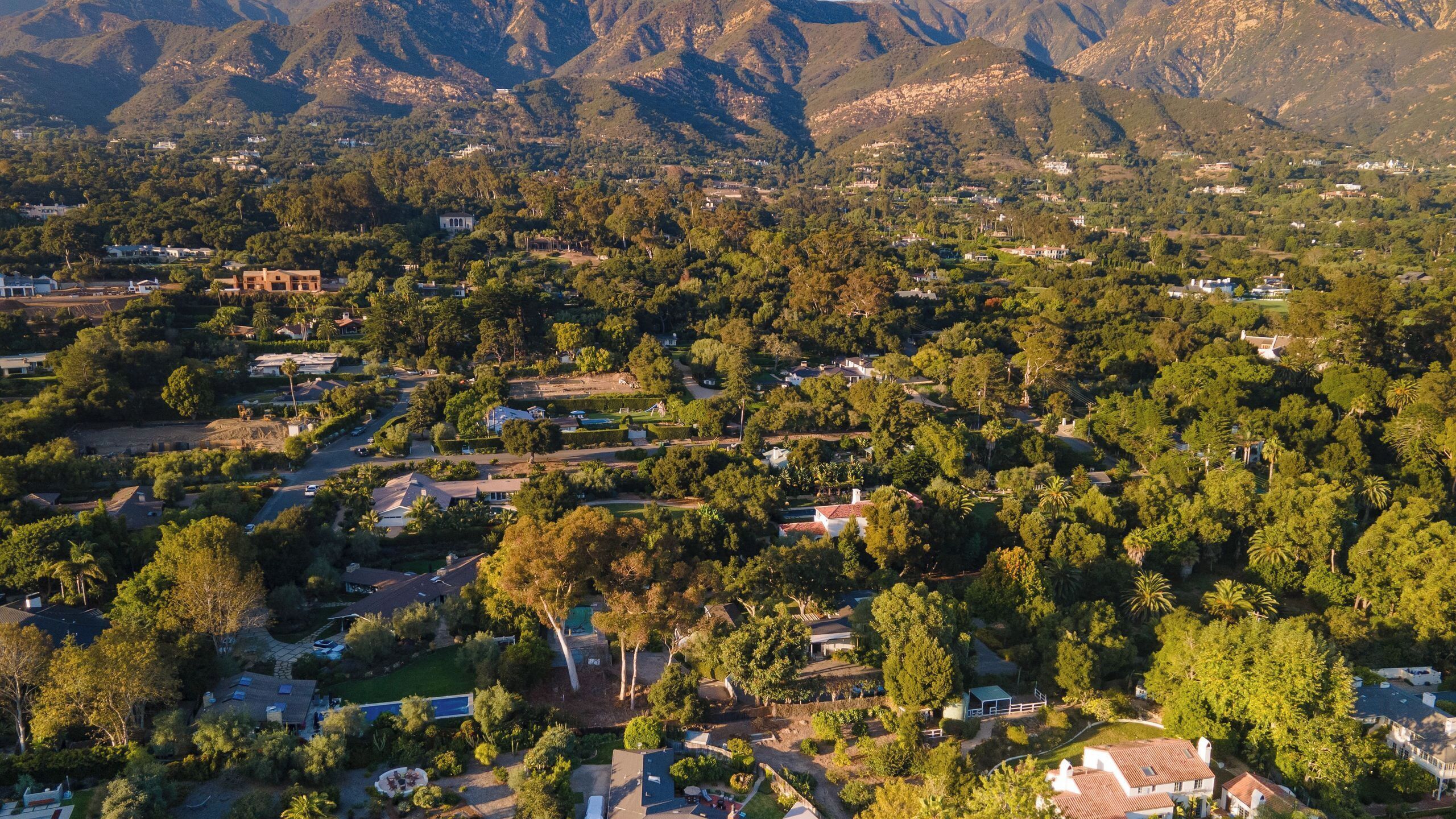 An aerial view of a residential area with houses, trees, and a mountainous backdrop.