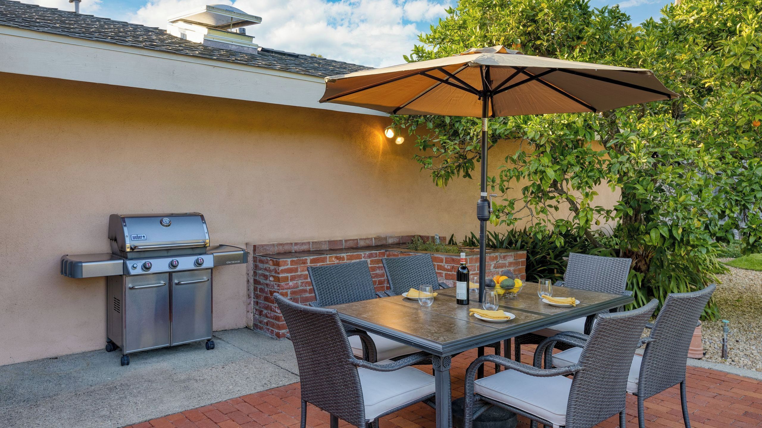 Eine Terrasse im Freien mit Grill, Tisch, Stühlen und Sonnenschirm.