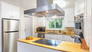 A modern kitchen with stainless steel appliances, a built-in oven, and a window with a view of greenery.