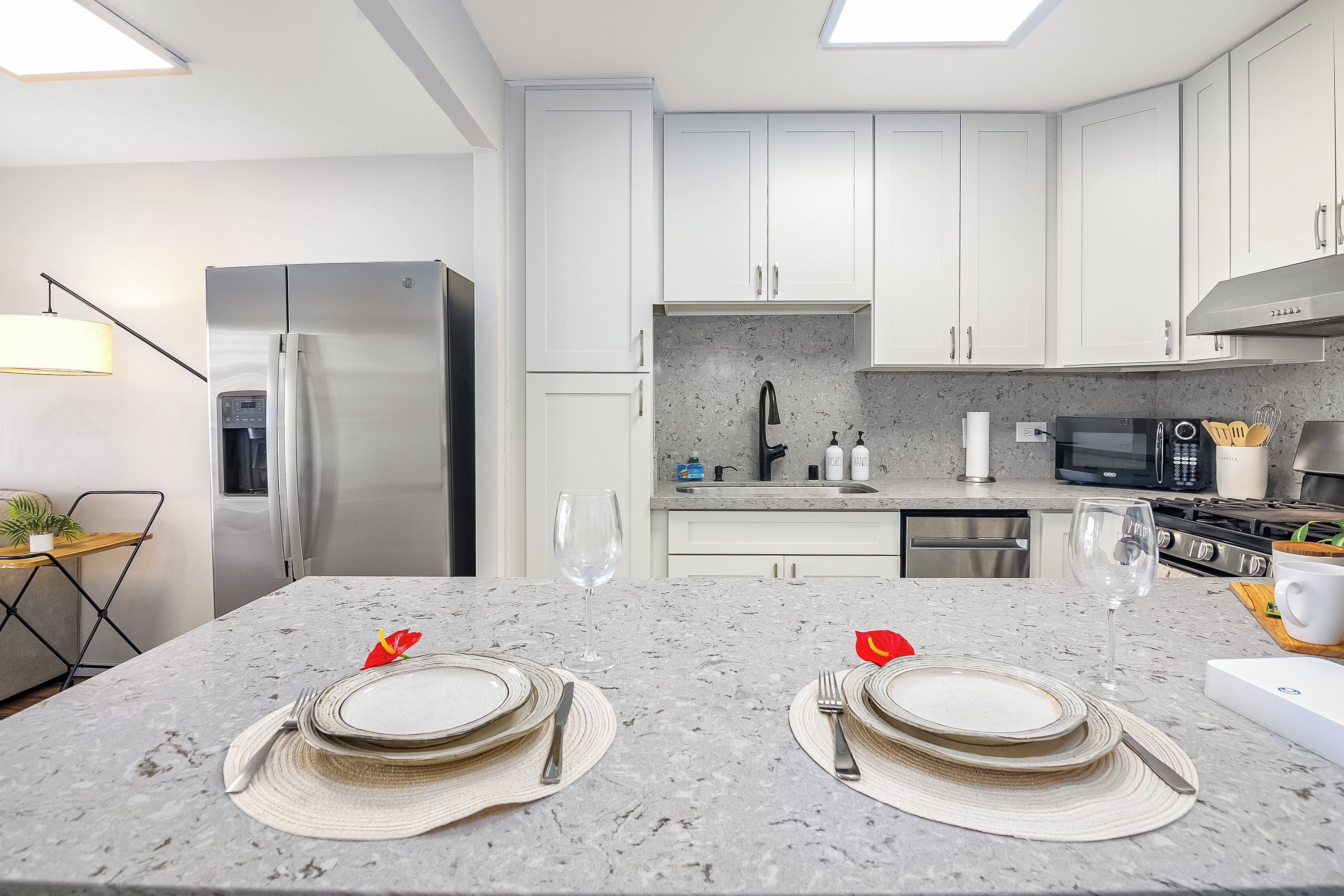 Une cuisine moderne avec des meubles blancs, un réfrigérateur en acier inoxydable et un plan de travail en granit.