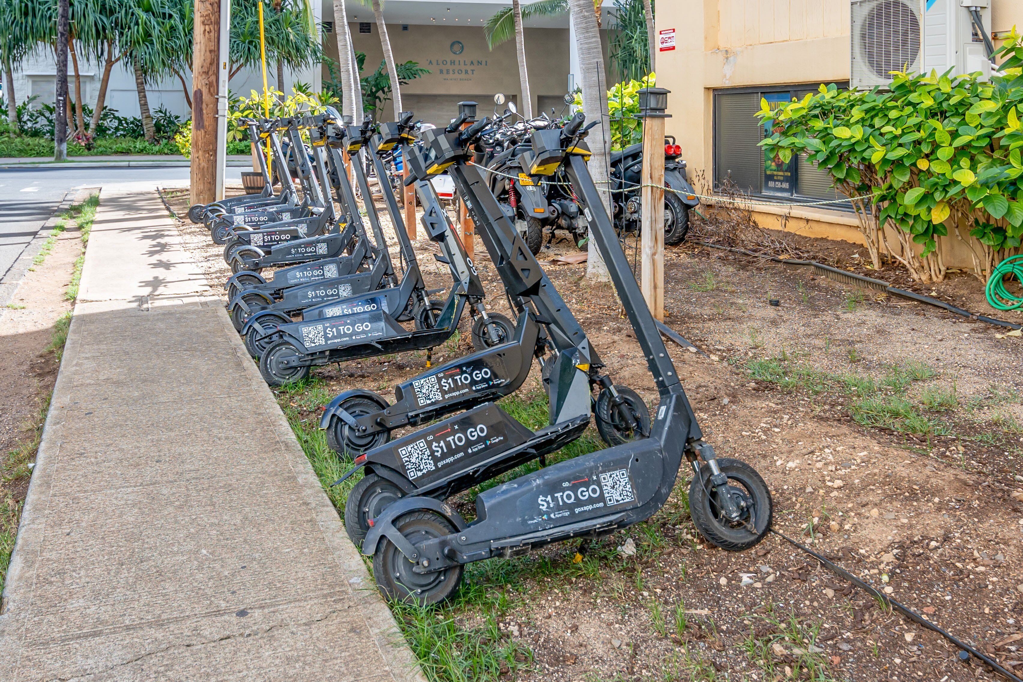 Een rij elektrische scooters geparkeerd op een stoep.
