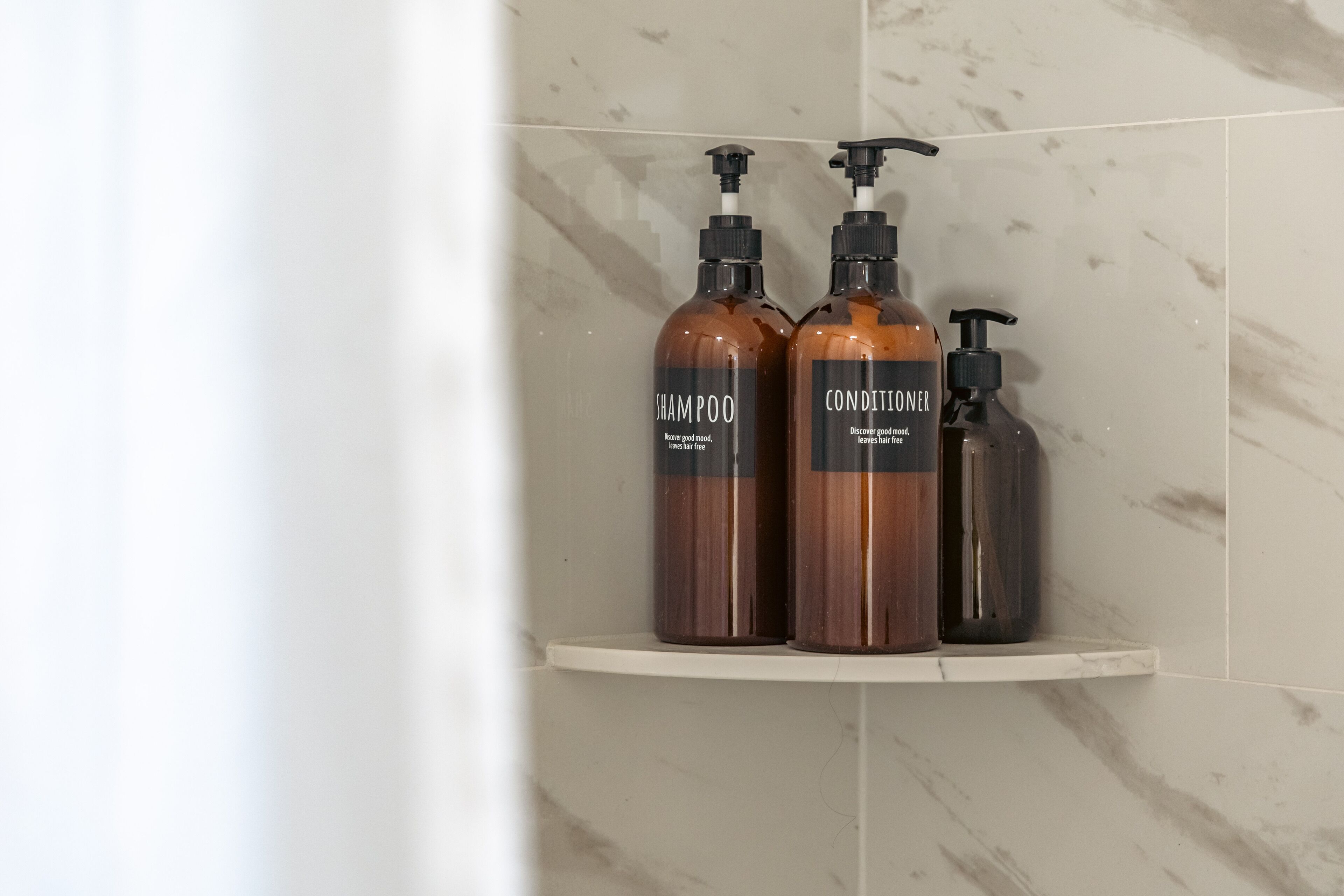Un baño con pared de mármol y estante que contiene tres botellas de champú y acondicionador.