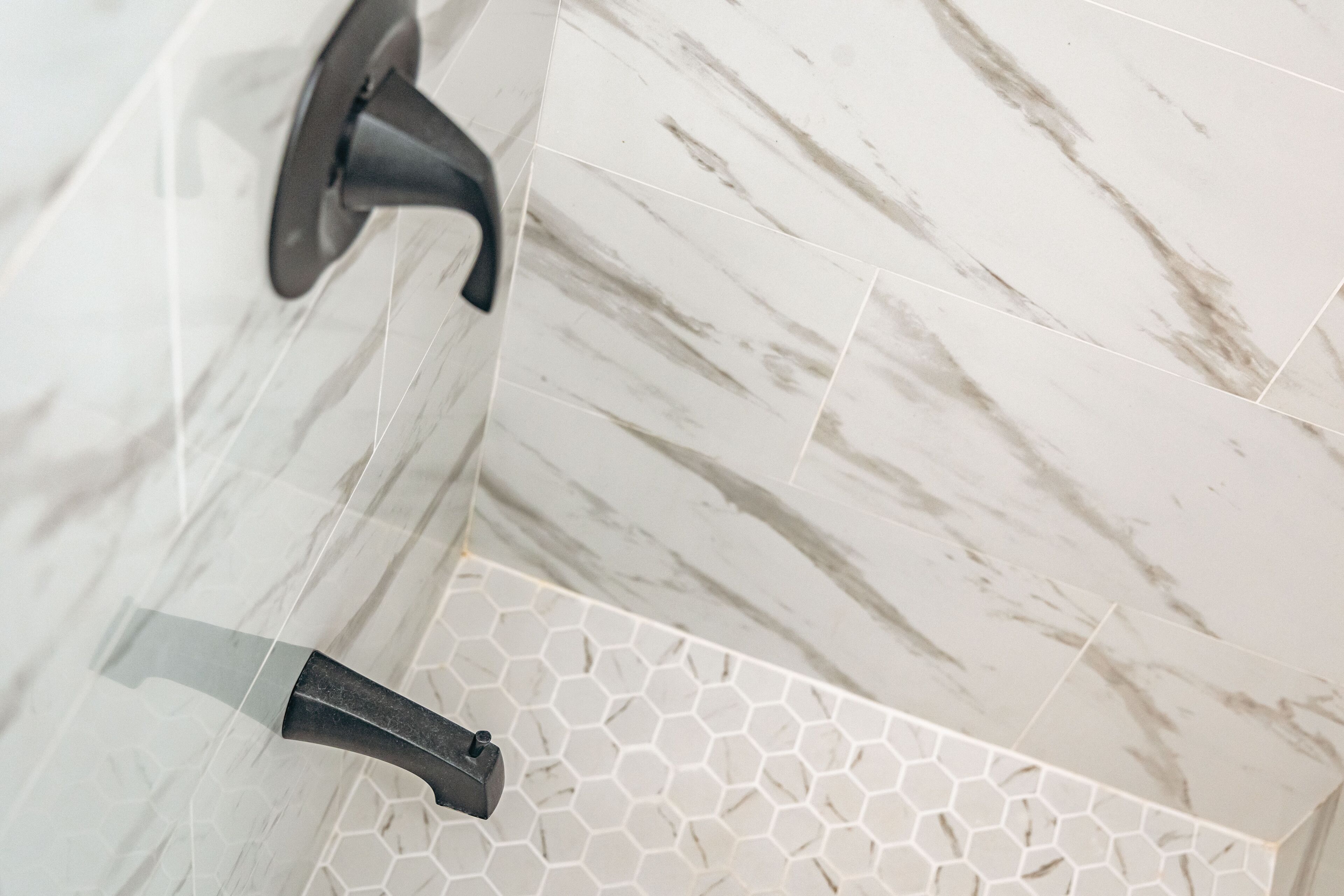 A bathroom with white marble tiles and a hexagonal tile pattern on the floor.
