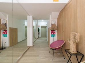 Un pasillo con espejo, una silla de mimbre, un reloj y un muro de madera.