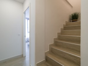 Una escalera de madera con peldaños que conducen a un rellano, donde hay una planta en maceta y una puerta que da a otra habitación.