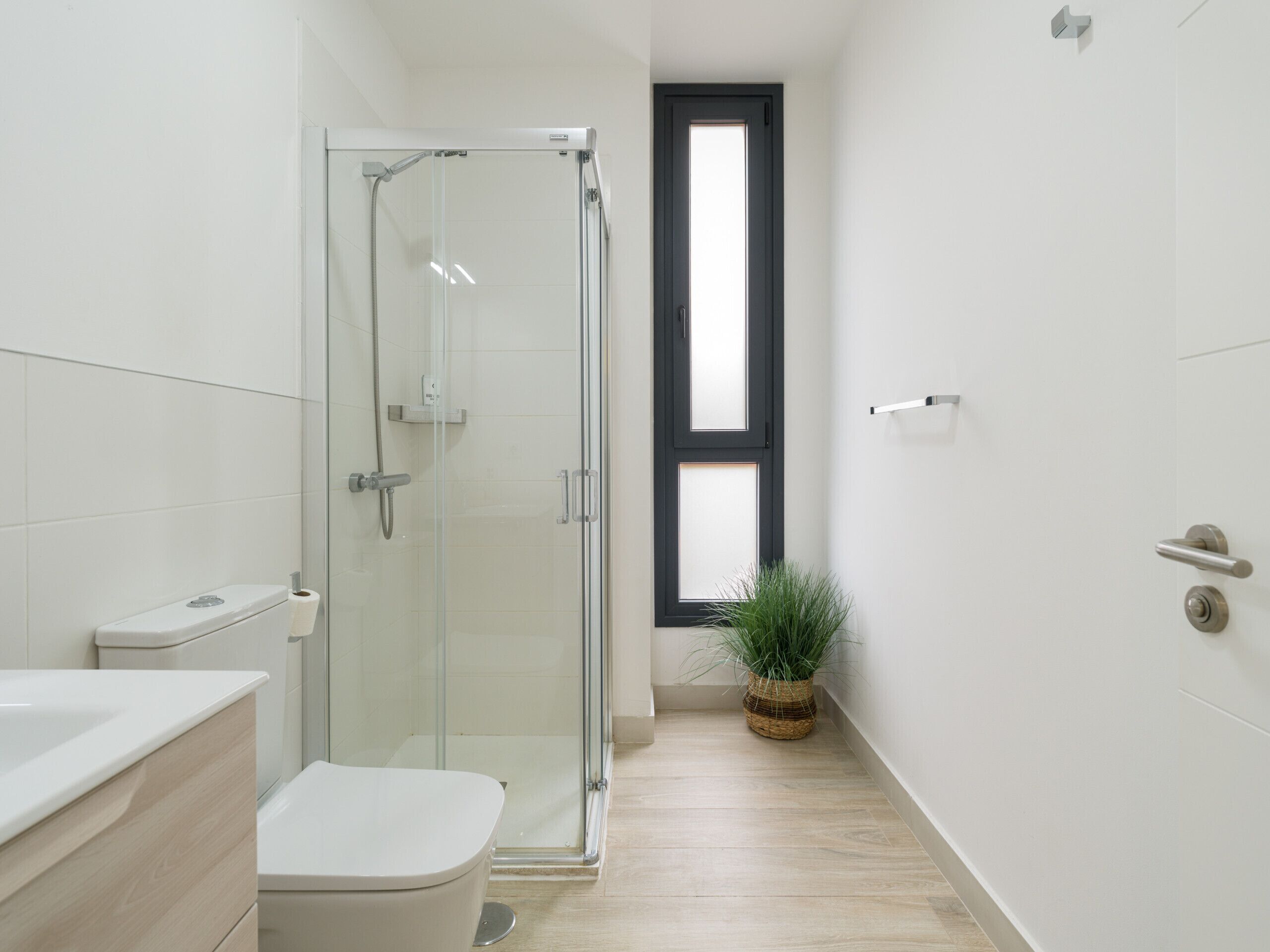 Un bagno moderno con box doccia in vetro, un water, un lavandino e una finestra.