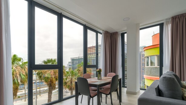 A modern living room with a dining area, large windows, and a view of the cityscape.