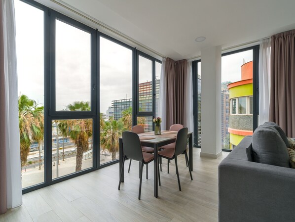 A modern living room with a dining area, large windows, and a view of the cityscape.
