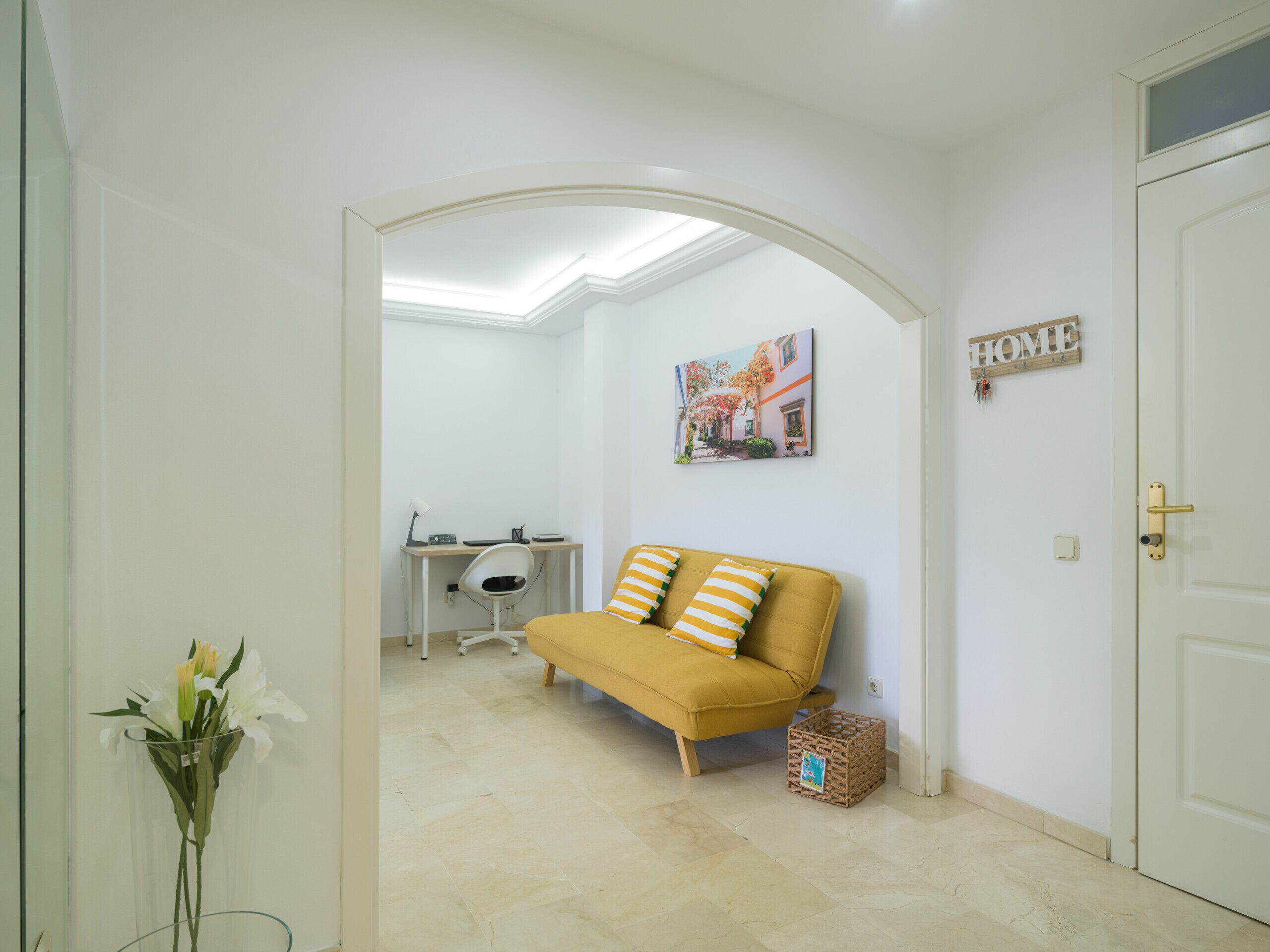 Una habitación con un sofá amarillo, un escritorio con una silla, un cuadro en la pared y un letrero que dice 'HOME'.