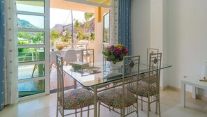 Zona pranzo con tavolo in vetro e sedie, un vaso con fiori e vista sulle montagne attraverso ampie finestre.