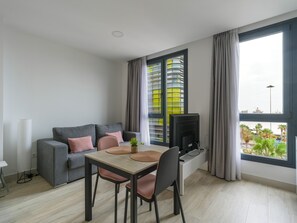 A modern living room with a grey sofa, a wooden dining table, and a TV.