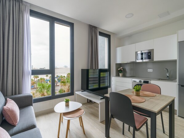 A modern apartment with a dining area, kitchen, and a large window offering a city view.