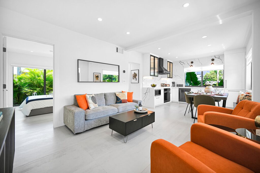 Un salon moderne avec un canapé, une table basse et des fauteuils orange. On y trouve également un coin repas avec une table et des chaises, ainsi qu’une cuisine équipée d’une cuisinière et de placards.