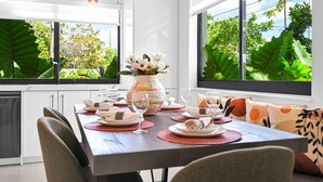 A modern dining area with a table set for four, large windows, and a view of greenery outside.