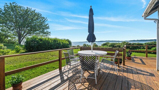 A wooden deck with a round table and chairs, a potted plant, and a view of the water.