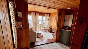 A wooden cabin interior with a large rug, a sofa, a small table, and a view of the outdoors.