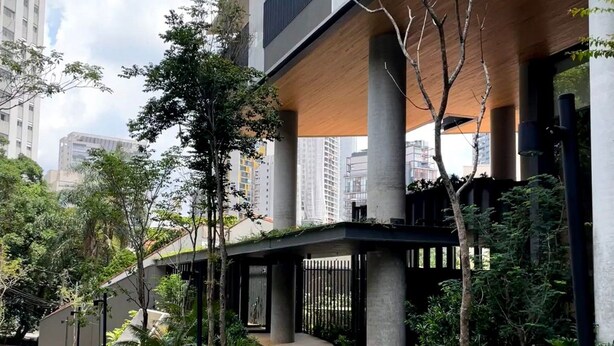 A modern building with a covered walkway, concrete pillars, and a mix of greenery and trees. - Vossa Bossa Agisse (São Paulo)