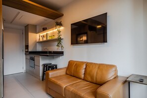 A modern kitchen with a built-in oven, a dining area with a brown leather sofa, and a mounted flat-screen TV. - Vossa Bossa Agisse (São Paulo)