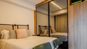 A hotel room with a bed, two chairs, a small table, and a large mirror. - Vossa Bossa Agisse (São Paulo)