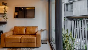 A modern living room with a leather sofa, a flat-screen TV, and a large window overlooking a balcony. - Vossa Bossa Agisse (São Paulo)