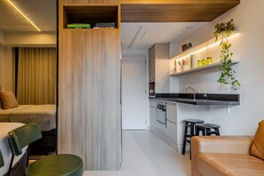 Une cuisine moderne dotée d’appareils électroménagers intégrés, un coin repas avec une chaise verte et un espace de vie avec un canapé.