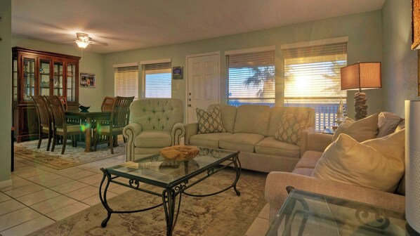 A living room with a glass coffee table, a sofa, a dining table with chairs, and a wooden cabinet. - Minutes to the Beach, Pool, Balcony w/ Nature Views Compass 17 by Avantstay (Corpus Christi)