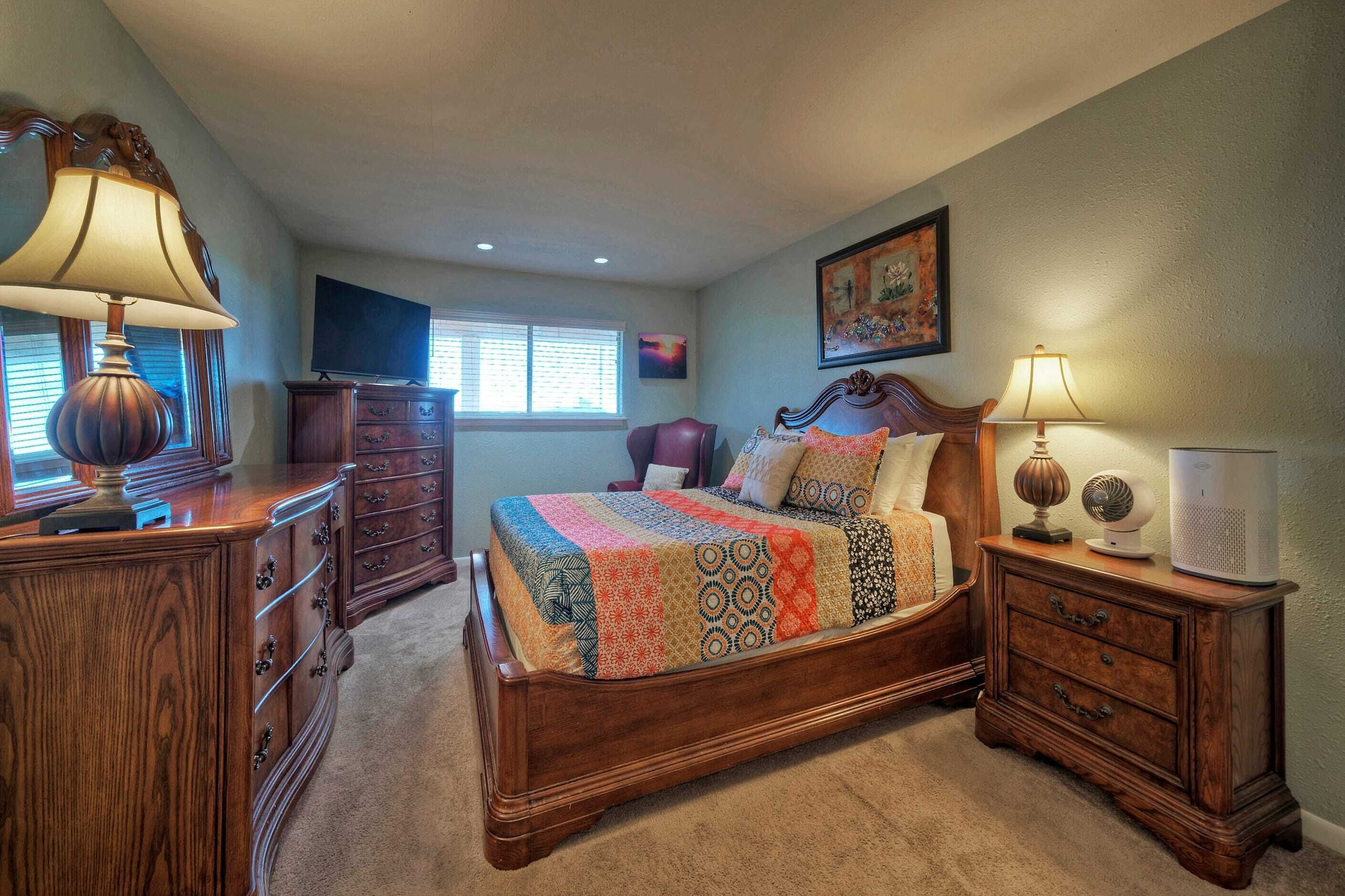 A bedroom with a wooden bed, a dresser, a nightstand, and a television.