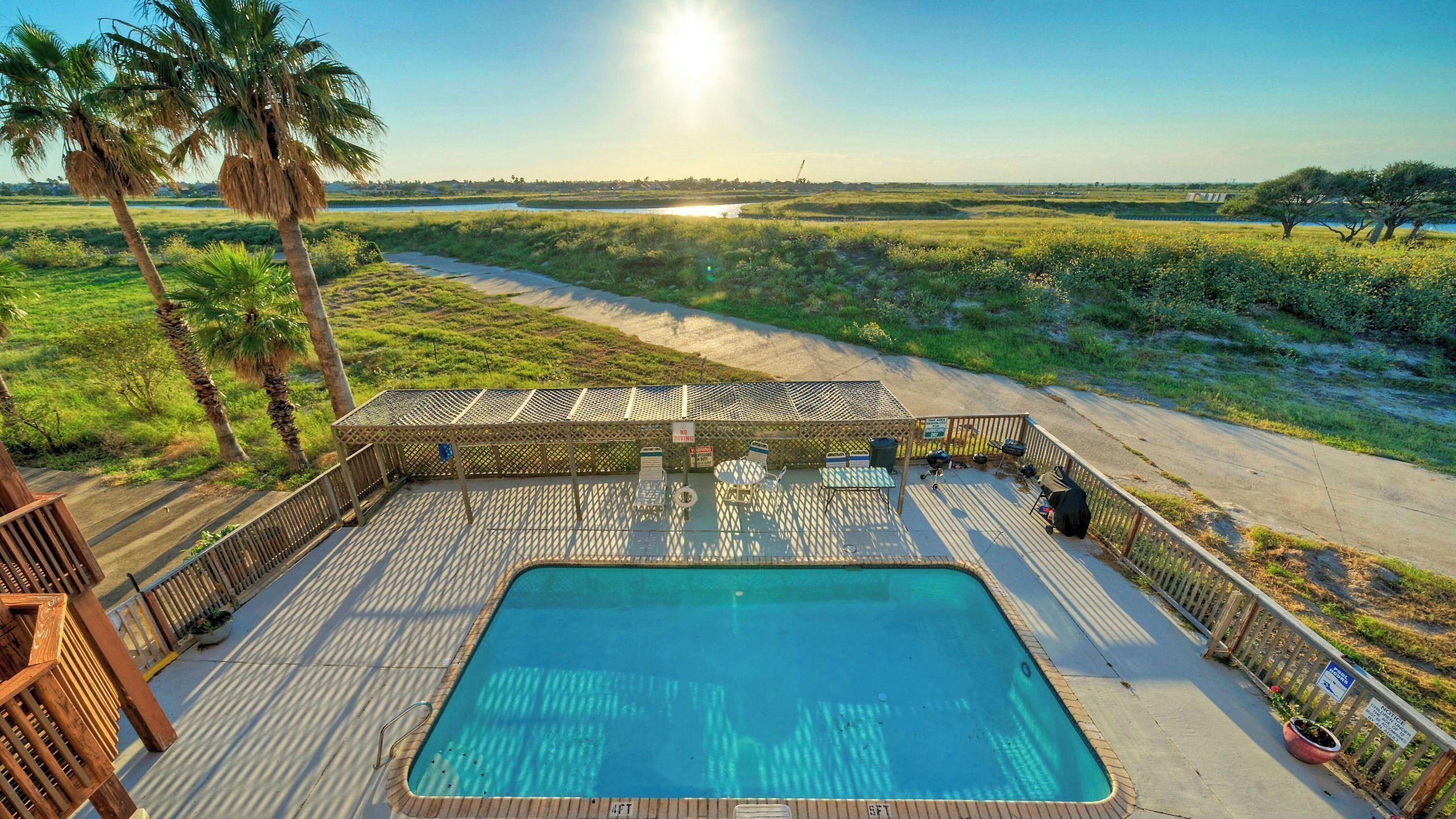 A pool area with a wooden deck, lounge chairs, and a view of the surrounding landscape.