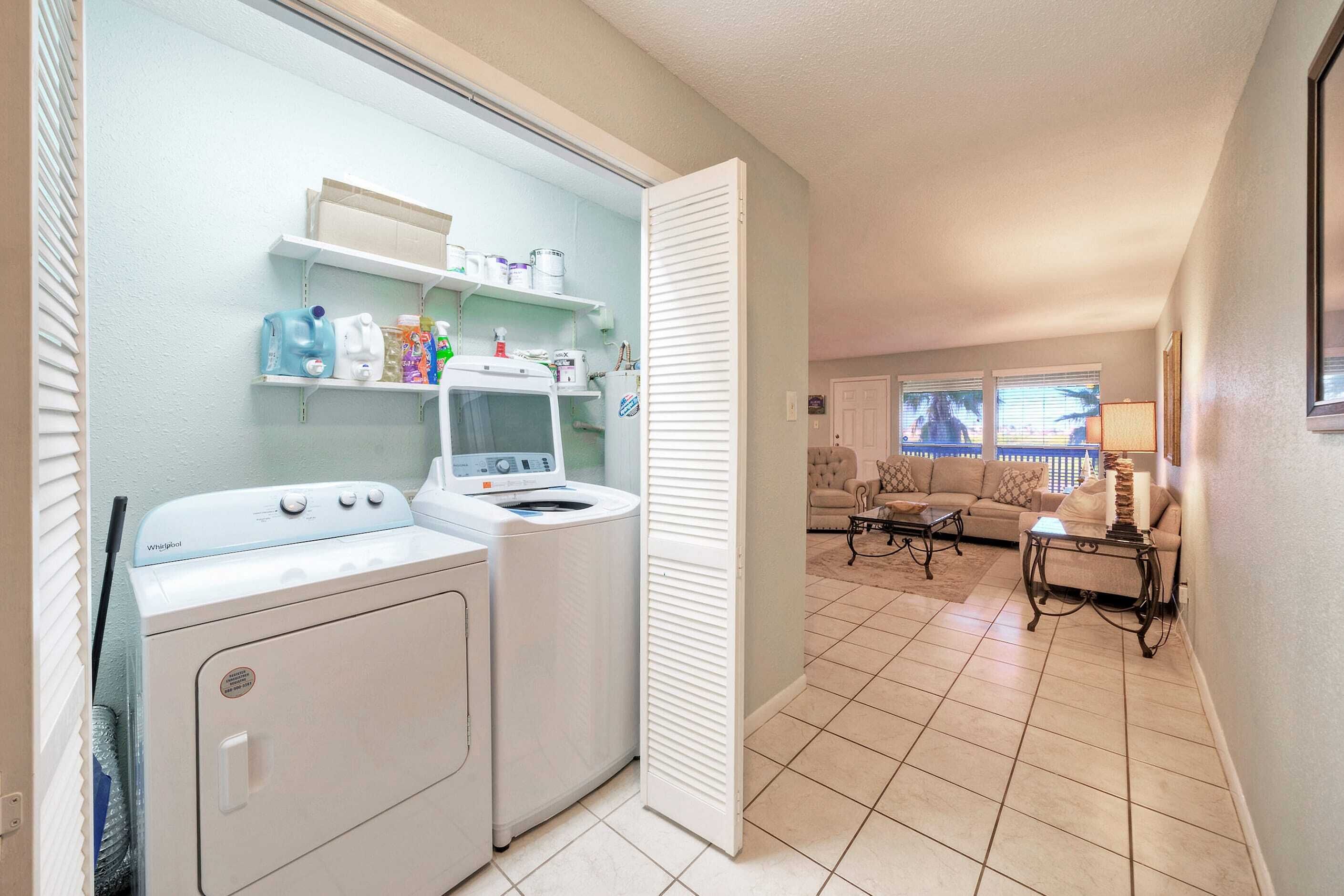 A laundry area with a washer and dryer, a shelf with cleaning supplies, and a living room with a sofa and coffee table.