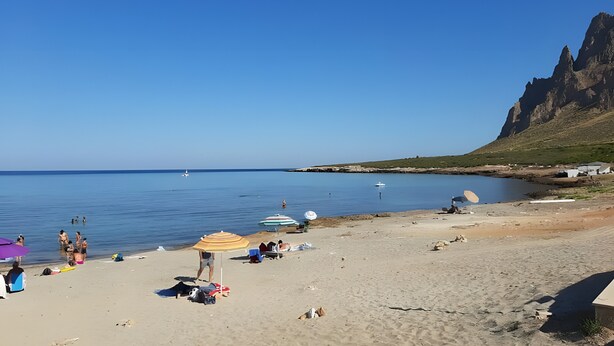 Een strand met mensen, parasols en boten.