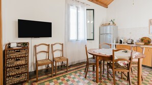 Een keuken met een houten plafond, een aan de muur bevestigde televisie, een koelkast en een eettafel met stoelen.