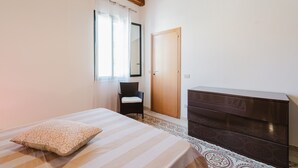 Een slaapkamer met een bed, een dressoir, een stoel, een raam met gordijnen en een houten plafond.