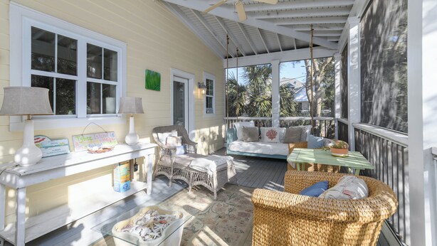 A sunlit porch with wicker furniture, a table with a plant, and a sign reading "Tybee Island is a real problem." - Screened Porches | Ping-Pong Table Pet-Friendly | Walk to Beach & Pier (Tybee Island)
