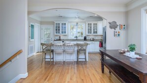 A kitchen with white cabinets, a wooden bench, and a dining table. - Screened Porches | Ping-Pong Table Pet-Friendly | Walk to Beach & Pier (Tybee Island)