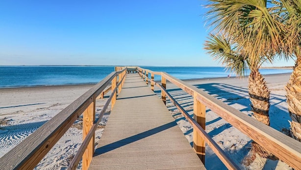 A wooden boardwalk leading to a beach with palm trees. - Pools + Tennis | Walk to Shops & Restaurants | Coastal Condo (Tybee Island)