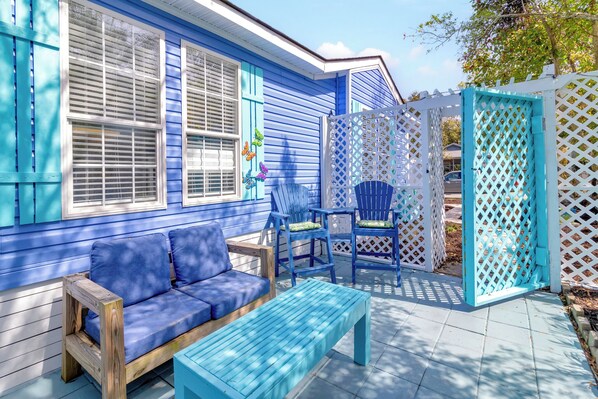 Ein blaues Haus mit einer Holzterrasse, einem blauen Sofa und einer passenden Bank.