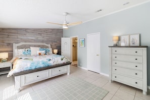 A bedroom with a bed, a dresser, a ceiling fan, and a door leading to another room. - Pet-Friendly w/ Fenced Yard | Easy Beach Access + Walk to Shops (Tybee Island)