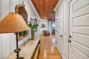 A hallway with a wooden ceiling, a bench with a lamp, a potted plant, and a door.