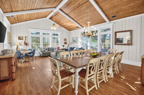 A spacious living area with a wooden ceiling, a dining table with chairs, and a sofa. - 7BR Family Retreat | Multiple Porches + Private Spaces For Everyone (Tybee Island)