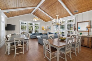 A spacious dining area with a wooden table and chairs, a living room with a sofa and a TV mounted on the wall.