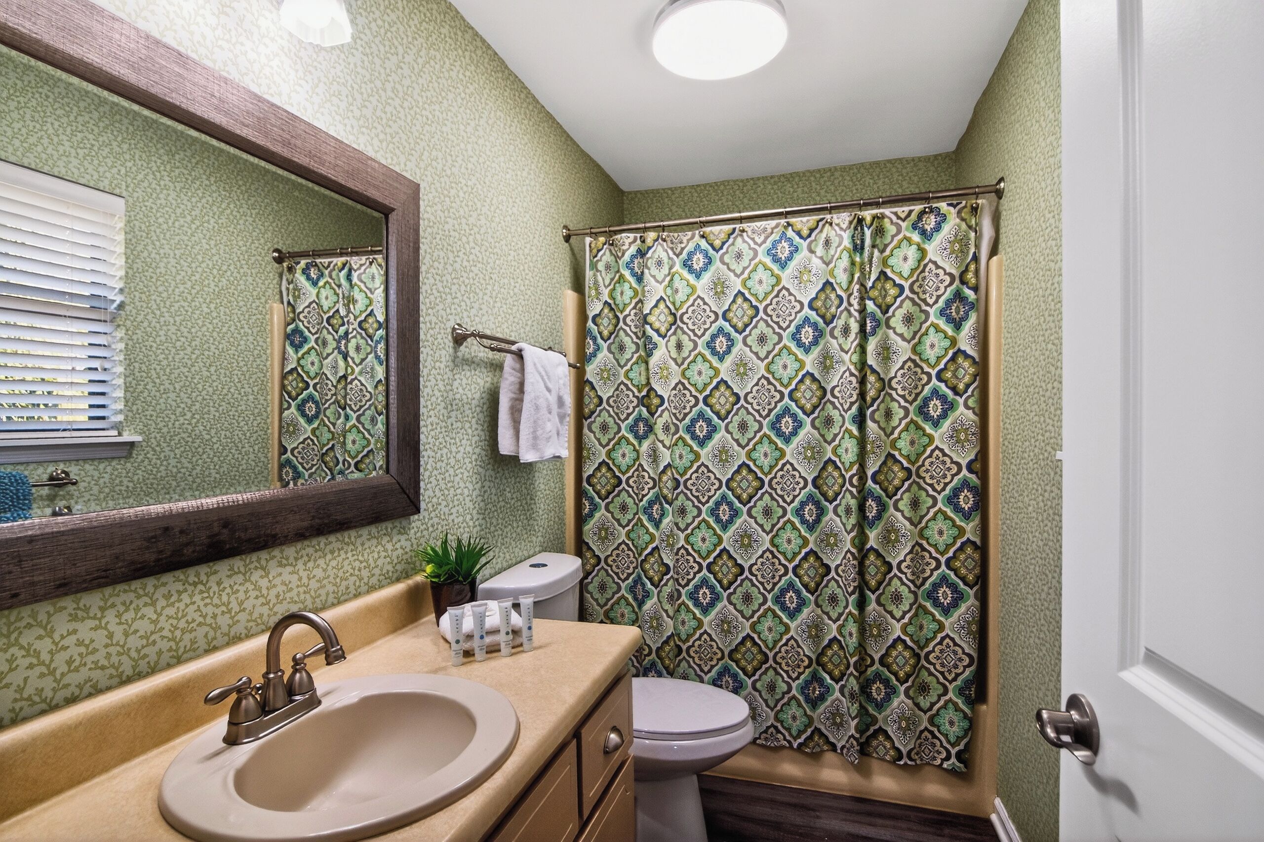 Une salle de bain équipée d’un lavabo, d’un miroir, de toilettes et d’un rideau de douche à motifs.