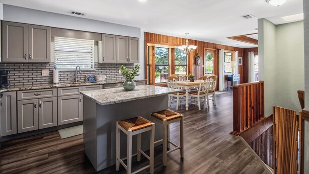 Una cocina moderna con una isla central, suelo de madera y un comedor con mesa y sillas de madera.