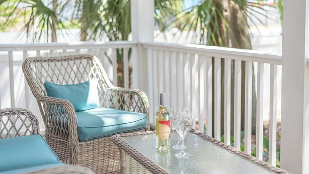 A wicker chair with a blue cushion, a bottle of wine, and two glasses on a glass table.