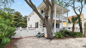 A two-story house with a porch, a white fence, and a tree in the foreground.