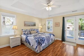 Une chambre à coucher avec un lit, des tables de chevet, un ventilateur de plafond et une vue sur l’extérieur.