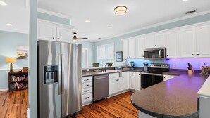 A modern kitchen with white cabinets, stainless steel appliances, and a wooden floor.